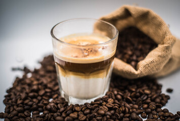 Dirty coffee menu in a clear glass placed on top of roasted coffee beans spilled on the floor.