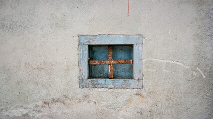 Pequeña ventana con reja oxidada en mro blanco con marco de madera azul  - obrazy, fototapety, plakaty