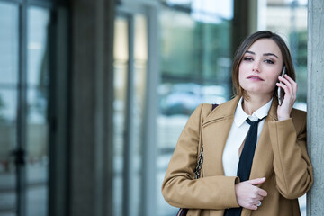 manager donna con cappotto beige , camicia bianca e cravatta nera cammina in contesto urbano utilizzando il suo smartphone