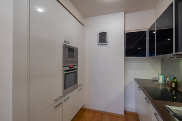 Contemporary interior of kitchen in luxury flat. Modern kitchen set. White walls. Built-in oven. Induction cooker.