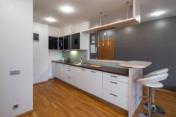 Contemporary interior of kitchen in luxury flat. Modern kitchen set with sink. Wooden counter. White walls. Bar stools.