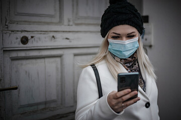 Fototapeta na wymiar Front photo of young woman reading a message while leaving house and wearing face mask