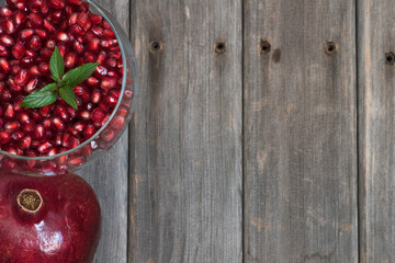  Arils with mint leaves in a glass bowl on a weathered board table top.  Fresh pomegranate.