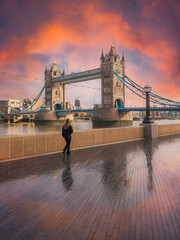 Beautiful scene with the historical Tower Bridge of London illuminated at sunrise and a person watching the scene