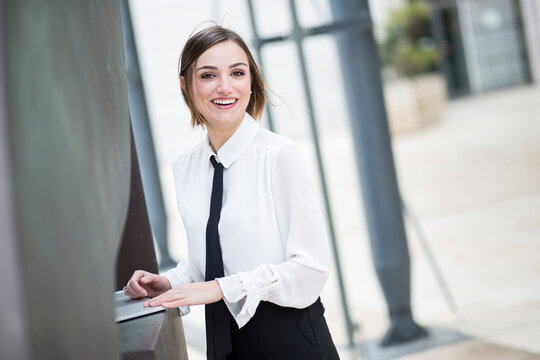 manager donna bionda con i capelli a caschetto, camicia bianca e cravatta nera, lavora al computer in esterni e sorride felice