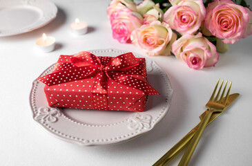Gift with red ribbon on a plate on white background and pink roses