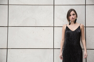 Bellissima ragazza con i capelli a caschetto e un abito nero corto con bretelle , guarda seria...