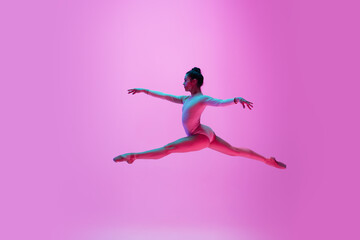 Fototapeta na wymiar Flying, jumping. Young and graceful ballet dancer on pink studio background in neon light. Art, motion, action, flexibility, inspiration concept. Flexible caucasian ballet dancer, moves in glow.