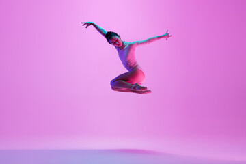 Flying, jumping. Young and graceful ballet dancer on pink studio background in neon light. Art, motion, action, flexibility, inspiration concept. Flexible caucasian ballet dancer, moves in glow.