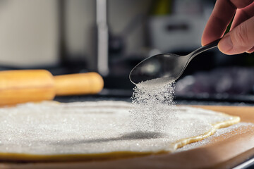 hand sprinkles sugar dough on the table. home cooking
