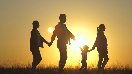 Silhouette of happy sevent, walking hand in hand, walks in field at sunset. Children hold hands of mom and dad. Happy little child and parents walk in rays of beautiful sun. Family travel on vacation