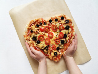 a child holds a heart shaped pizza made with his own hands. February 14 and mom's day holiday...