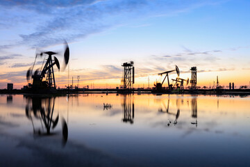 Obraz premium in the evening, oil pumps are running, The oil pump and the beautiful sunset reflected in the water, the silhouette of the beam pumping unit in the evening.