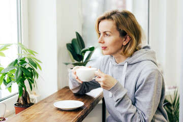 A woman is drinking coffee with pleasure in a light coffee shop by the window.