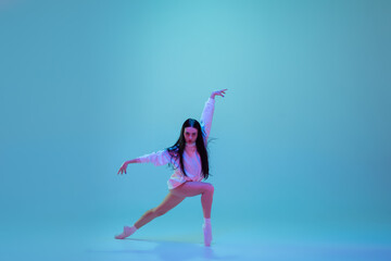 Naklejka na ściany i meble Strong. Young and graceful ballet dancer isolated on blue studio background in neon light. Art, motion, action, flexibility, inspiration concept. Flexible caucasian ballet dancer, moves in glow.