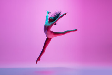 Flying, freedom. Young and graceful ballet dancer on pink studio background in neon light. Art,...