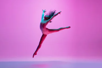 Gordijnen Flying, freedom. Young and graceful ballet dancer on pink studio background in neon light. Art, motion, action, flexibility, inspiration concept. Flexible caucasian ballet dancer, moves in glow. © master1305