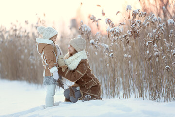 Fototapeta na wymiar two little sisters in winter clothes walk and play in a snow park. Winter fun