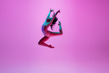 High above. Young and graceful ballet dancer on pink studio background in neon light. Art, motion, action, flexibility, inspiration concept. Flexible caucasian ballet dancer, moves in glow. - obrazy, fototapety, plakaty