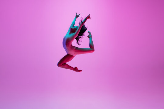 High above. Young and graceful ballet dancer on pink studio background in neon light. Art, motion, action, flexibility, inspiration concept. Flexible caucasian ballet dancer, moves in glow. - Powered by Adobe