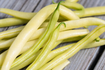Yellow raw wax beans texture close up, a pile of freshly harvested ripe long pods on a gray wooden background