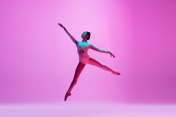 Flying, freedom. Young and graceful ballet dancer on pink studio background in neon light. Art, motion, action, flexibility, inspiration concept. Flexible caucasian ballet dancer, moves in glow.