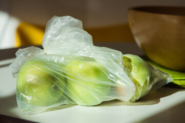 Green apples in a plastic shopping bag, on the kitchen table.
