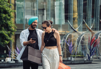 Indian boyfriend embrace his smiling girlfriend and showing his smartphone. Consumerism concept with copy space