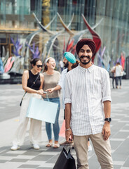 Handsome Indian man smiling, looking at camera and holding paper bag outdoors