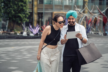 Beautiful mix raced couple using digital tablet and holding shopping bags outside shopping mall