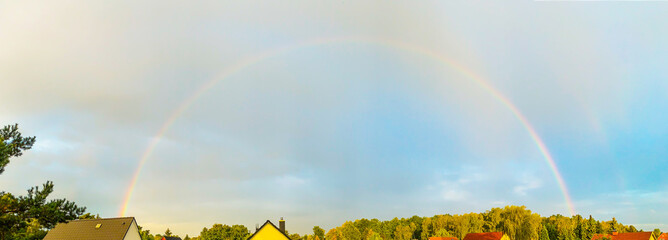 Ein kompletter Regenbogen steht am Himmel über Häusern und Bäumen