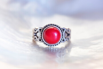 Antique silver ring with red coral mineral stone on white shell background