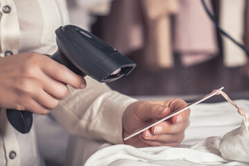 A warehouse woman employee accepts clothes using barcode scanner reading a bar code from price tag of female blouse and adds to the computer base