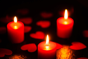 Three red burning candles. Candles with hearts. The background for the greeting card. A greeting card for Valentine's Day. February 14 is valentine's day. Used as a background or texture, soft focus