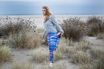 ragazza bionda con abbigliamento sportivo fa stretching in contesto naturale vicino al mare