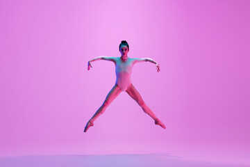 Fototapeta na wymiar Flying on. Young and graceful ballet dancer on pink studio background in neon light. Art, motion, action, flexibility, inspiration concept. Flexible caucasian ballet dancer, moves in glow.