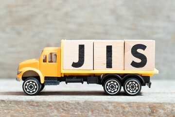 Fototapeta premium Toy truck hold alphabet letter block in word JIS (abbreviation of Just in sequence) on wood background
