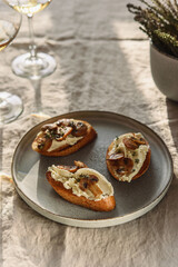 Bruschettas or toasts with cheese and fried mushrooms with thyme served with glasses of wine on greige linen tablecloth