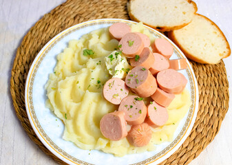 Mashed potatoes with sausages on a plate and white bread next to it.