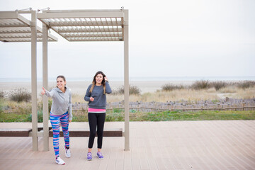 amiche in abbigliamento casual fanno l'autostop con espressione divertita , vicino a una pensilina dell'autobus