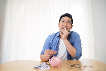 Happy man holding piggy bank,Asian man in casual shirt putting money in piggy bank