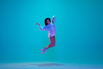 Obraz na płótnie Canvas Flying. Young and graceful ballet dancer isolated on blue studio background in neon light. Art, motion, action, flexibility, inspiration concept. Flexible caucasian ballet dancer, moves in glow.