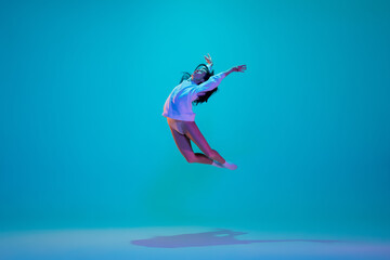 Obraz na płótnie Canvas Flying. Young and graceful ballet dancer isolated on blue studio background in neon light. Art, motion, action, flexibility, inspiration concept. Flexible caucasian ballet dancer, moves in glow.
