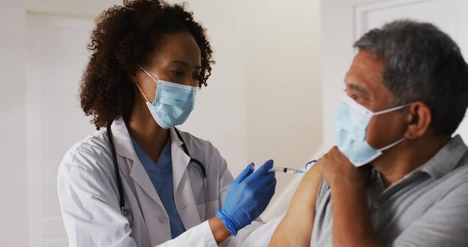 Mixed race female doctor wearing mask giving vaccination to senior man at home