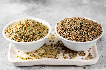 Hemp seeds. Peeled and whole dried hemp seeds in a white ceramic bowl on a light gray kitchen table. Hemp Seeds for Cooking