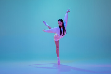 Naklejka na ściany i meble Inspired. Young and graceful ballet dancer isolated on blue studio background in neon light. Art, motion, action, flexibility, inspiration concept. Flexible caucasian ballet dancer, moves in glow.
