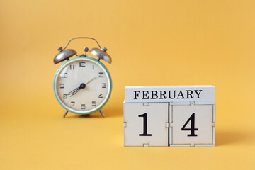 Calendar for February 14: cubes with the number 14 and the name of the month, alarm clock on a yellow background