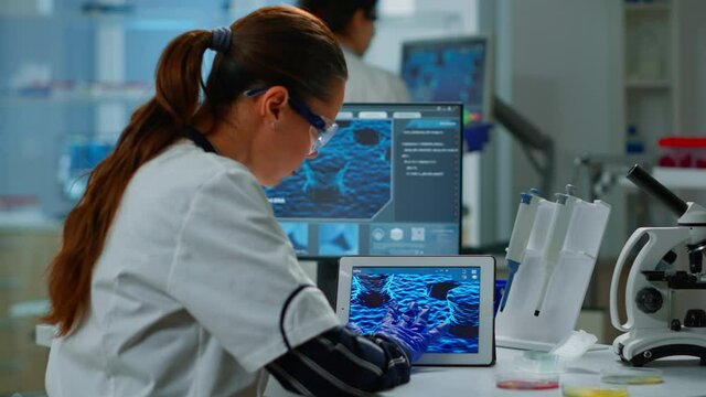 Scientist using digital tablet working in modern medical research laboratory, analyzing DNA information. Medicine, biotechnology research in advanced pharma lab, examining virus evolution