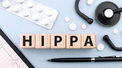 Wooden block form the word HIPAA Health Insurance Portability and Accountability Act on blue background with stethoscope, pills, capsules, pen and cardiogram. Medical concept. Flat lay, top view.