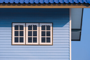 Sunlight on surface of 3 white windows on blue wooden wall of vintage house against blue sky background